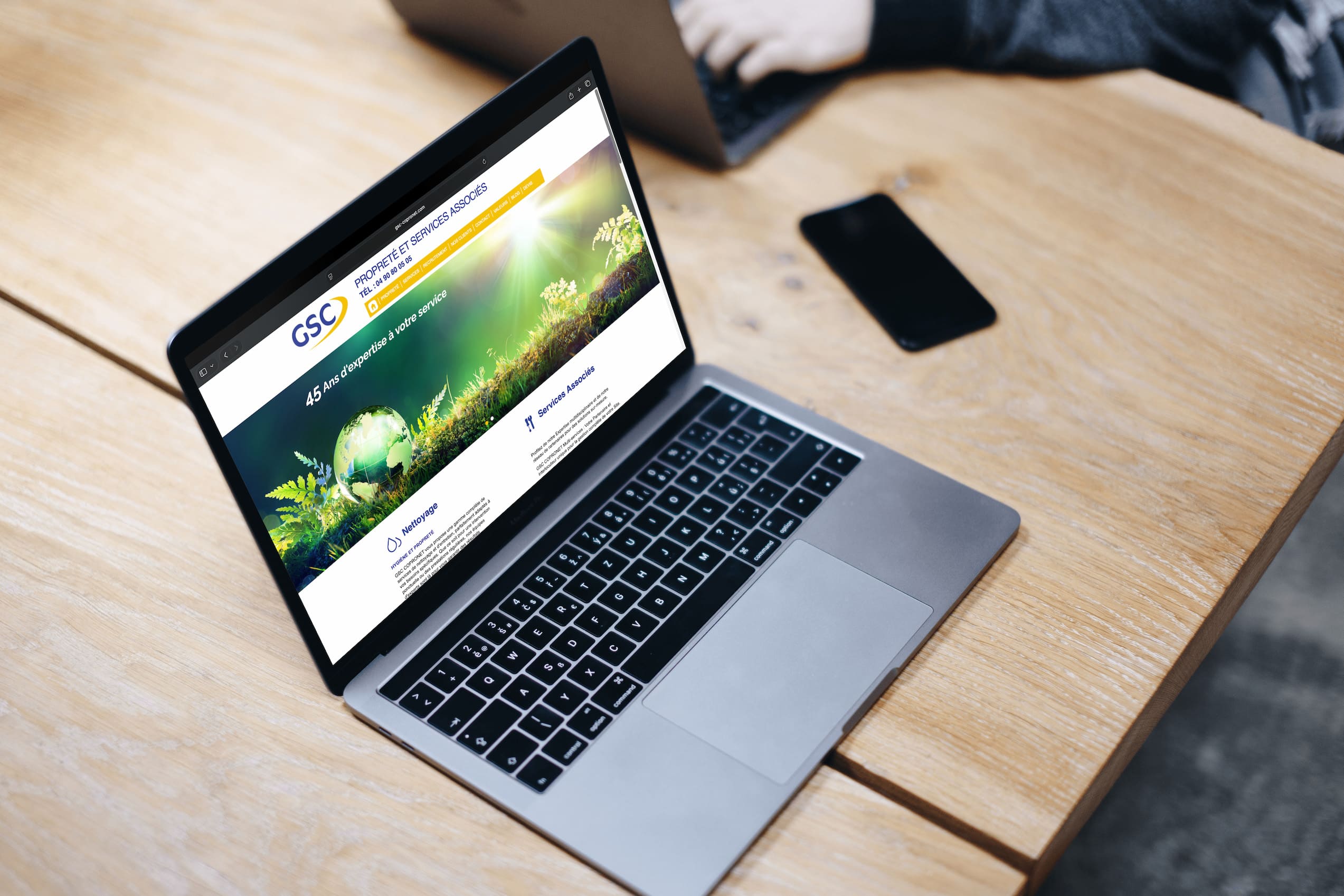 Vue de bureau créatif avec MacBook Pro affichant un design web, carnet de croquis géométrique et vue sur Avignon, illustrant l'écosystème digital complet du projet GSC Copronet.